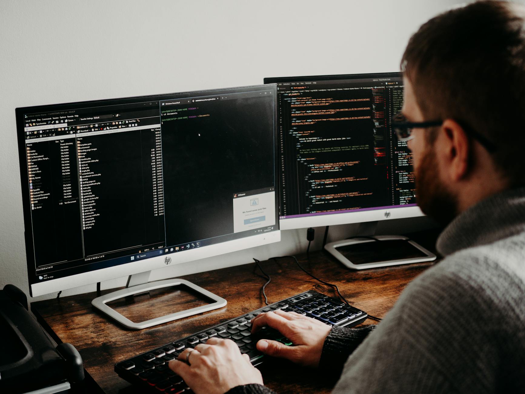 Programista przy biurku z dwoma monitorami w domowym biurze IT