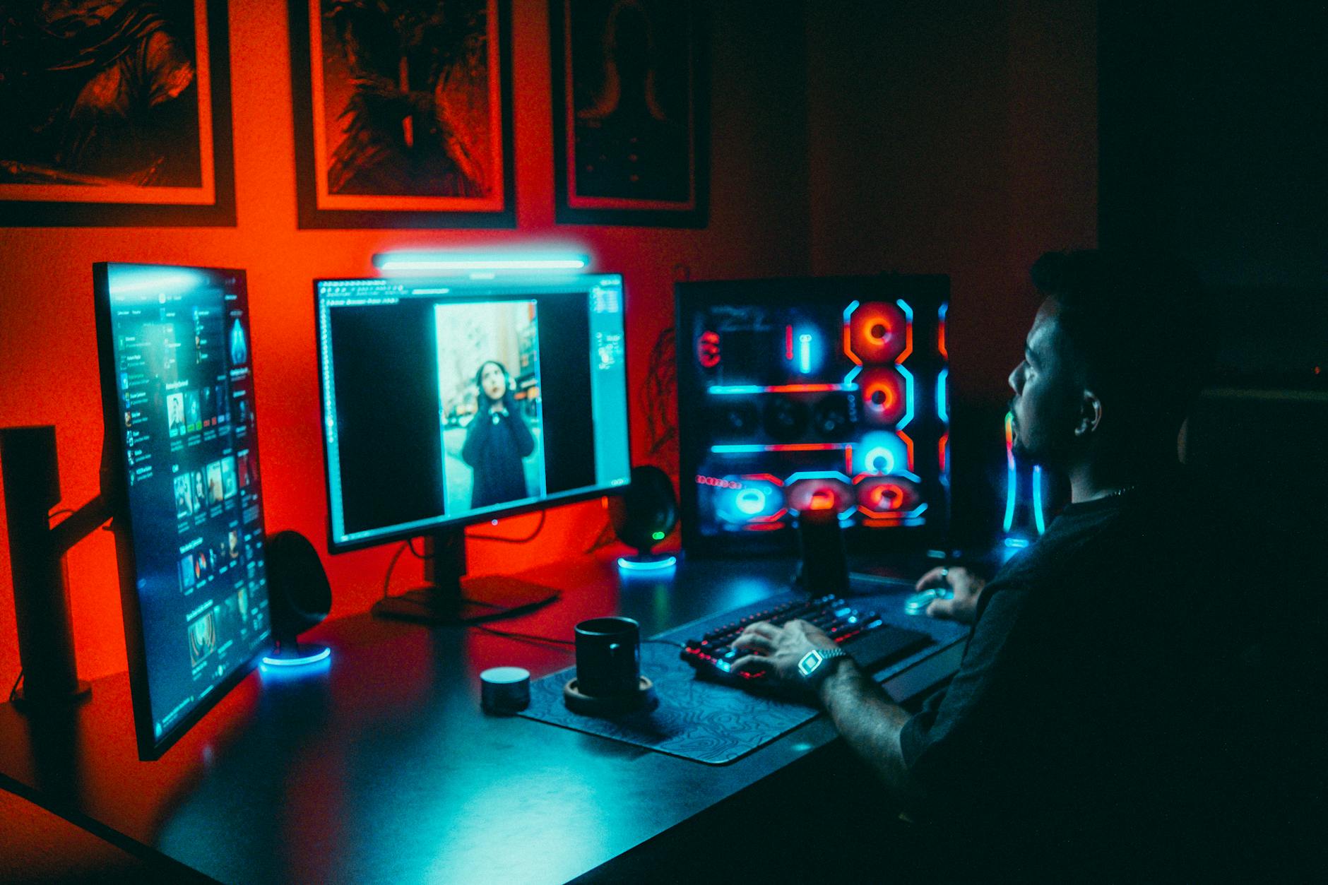 Młody programista pracuje nad grą na kilku monitorach w ciemnym pokoju