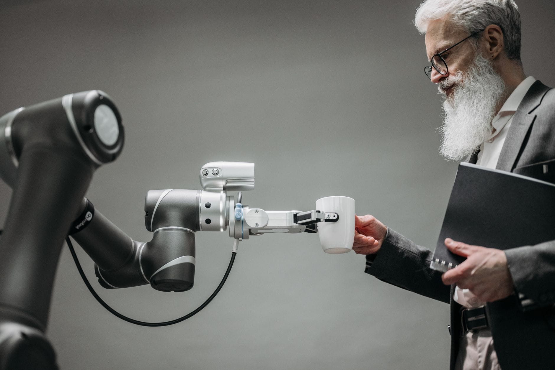 Starszy mężczyzna odbiera kubek od ramienia robota w biurze